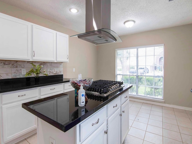 kitchen with tasteful backsplash, light tile patterned floors, white cabinetry, island range hood, and stainless steel gas cooktop