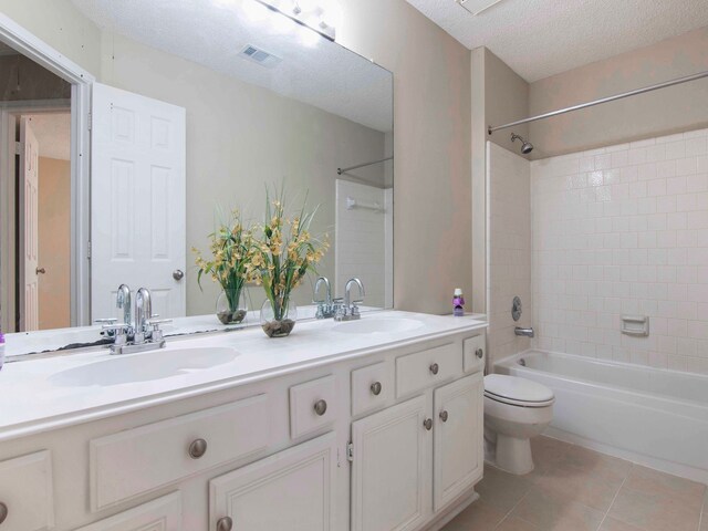 full bathroom with tiled shower / bath, a textured ceiling, toilet, vanity, and tile patterned floors