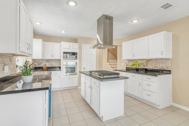 5635 Sage Manor Dr, Houston, TX 77084 - kitchen featuring backsplash, island range hood, appliances with stainless steel finishes, and white cabinetry