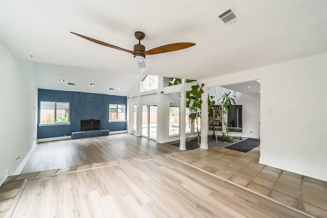 unfurnished living room with a fireplace, vaulted ceiling, a wealth of natural light, and ceiling fan