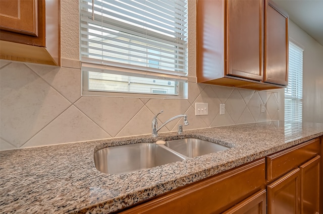 kitchen featuring plenty of natural light, light stone counters, sink, and decorative backsplash