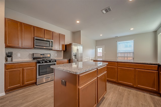 kitchen featuring light stone countertops, tasteful backsplash, light hardwood / wood-style floors, a center island, and stainless steel appliances