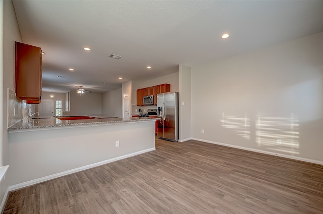 kitchen featuring stainless steel appliances, light stone counters, kitchen peninsula, ceiling fan, and light hardwood / wood-style floors