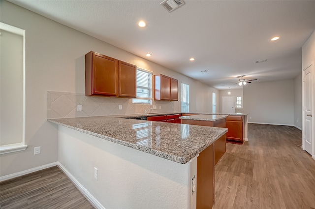 kitchen with backsplash, kitchen peninsula, light wood-type flooring, and ceiling fan