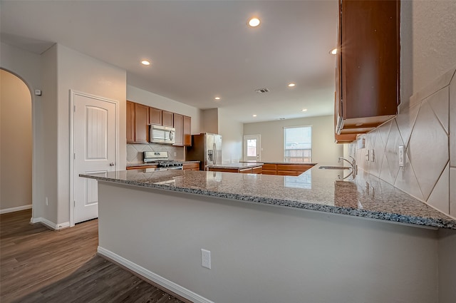 kitchen with backsplash, hardwood / wood-style flooring, stainless steel appliances, and kitchen peninsula