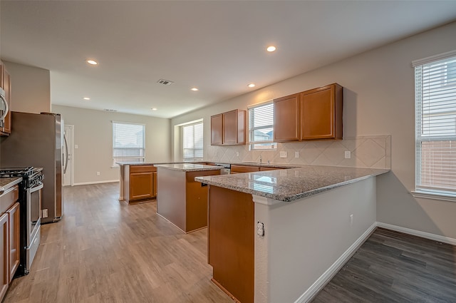 kitchen featuring light wood-type flooring, tasteful backsplash, kitchen peninsula, a center island, and appliances with stainless steel finishes