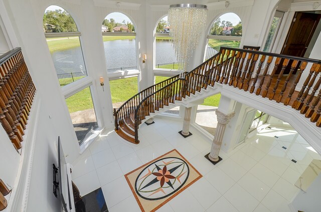 interior space featuring a towering ceiling, a water view, a chandelier, and tile patterned floors