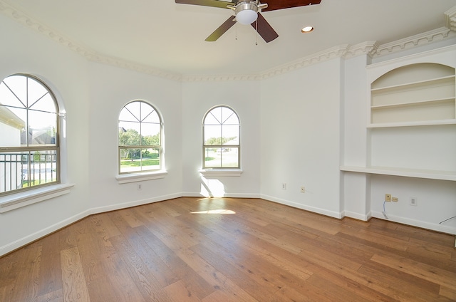 empty room with ornamental molding, built in features, wood-type flooring, and ceiling fan