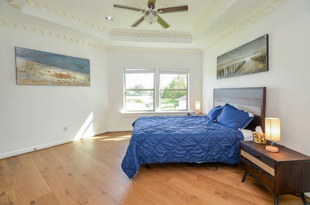 bedroom with crown molding, a raised ceiling, hardwood / wood-style flooring, and ceiling fan