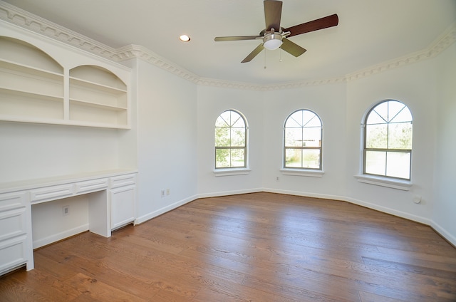 unfurnished office with built in desk, ceiling fan, and wood-type flooring