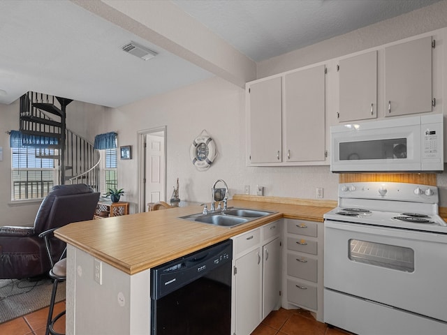 kitchen featuring light tile patterned flooring, white cabinetry, white appliances, sink, and kitchen peninsula