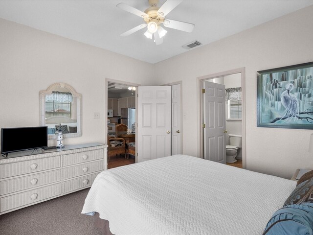 carpeted bedroom featuring ceiling fan, multiple windows, stainless steel fridge, and ensuite bathroom