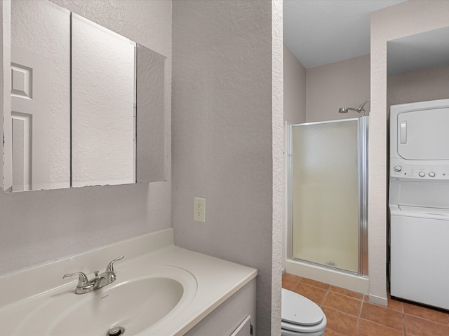 bathroom with walk in shower, stacked washer and clothes dryer, vanity, tile patterned floors, and toilet