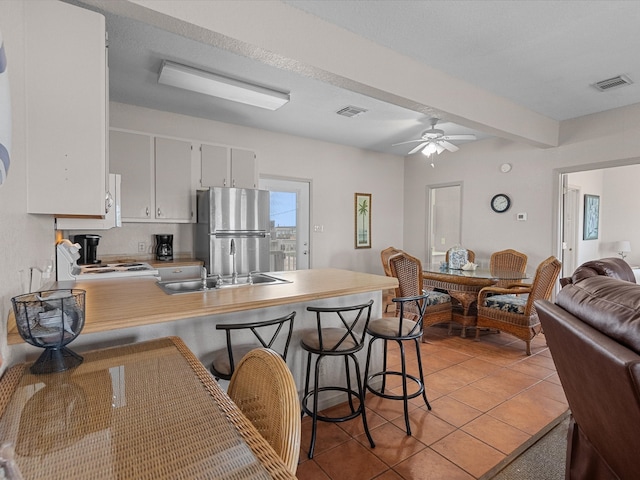 kitchen with light tile patterned flooring, beamed ceiling, kitchen peninsula, a kitchen breakfast bar, and stainless steel fridge