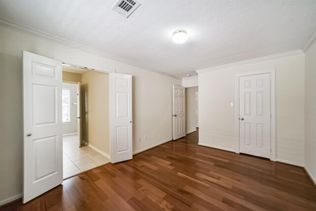 unfurnished bedroom with crown molding, wood finished floors, visible vents, and baseboards