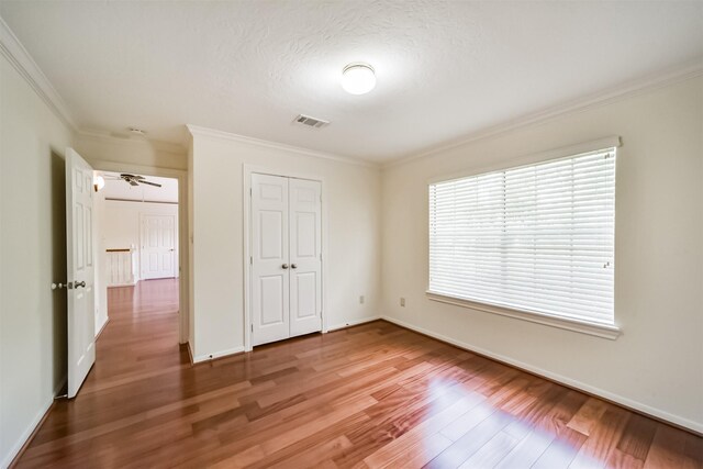 unfurnished bedroom featuring wood finished floors, baseboards, visible vents, ornamental molding, and a closet