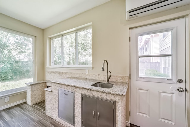 kitchen with a wall unit AC, baseboards, a sink, light stone counters, and wood finished floors