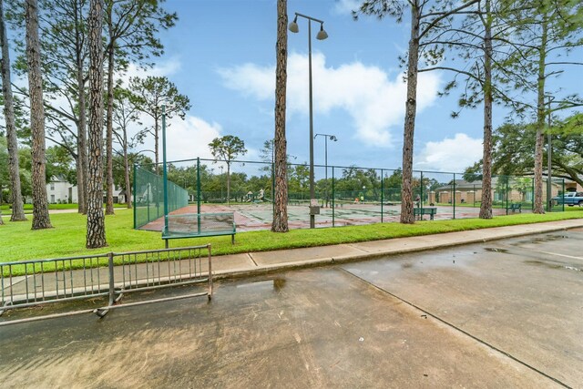 view of community featuring a tennis court, a yard, and fence