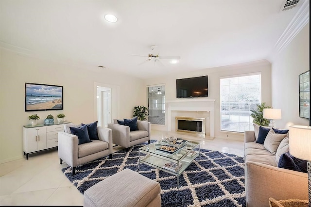 living area featuring light tile patterned flooring, visible vents, crown molding, a ceiling fan, and a glass covered fireplace
