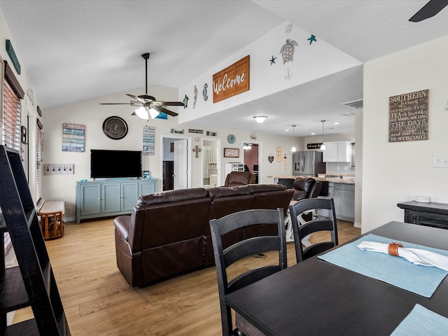 living area with ceiling fan, vaulted ceiling, a textured ceiling, and light wood-style flooring