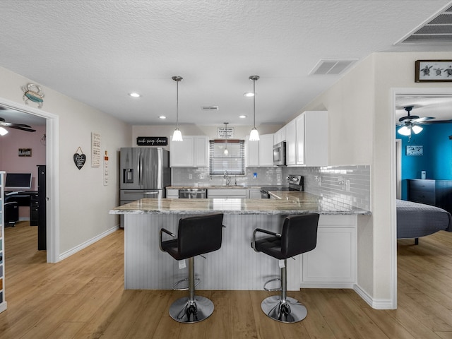 kitchen featuring decorative light fixtures, stainless steel appliances, visible vents, white cabinetry, and a peninsula