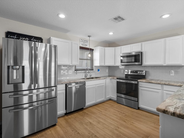 kitchen with a sink, visible vents, white cabinets, hanging light fixtures, and appliances with stainless steel finishes