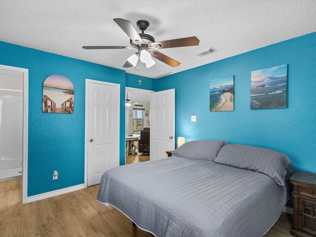 bedroom with a textured ceiling, a textured wall, ceiling fan, visible vents, and light wood-type flooring