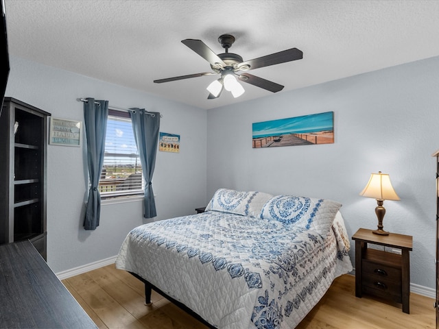 bedroom featuring baseboards, ceiling fan, a textured ceiling, and light wood-style floors