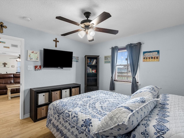 bedroom with light wood finished floors, ceiling fan, visible vents, and a textured ceiling