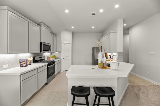 kitchen with appliances with stainless steel finishes, a breakfast bar, tasteful backsplash, gray cabinets, and light colored carpet