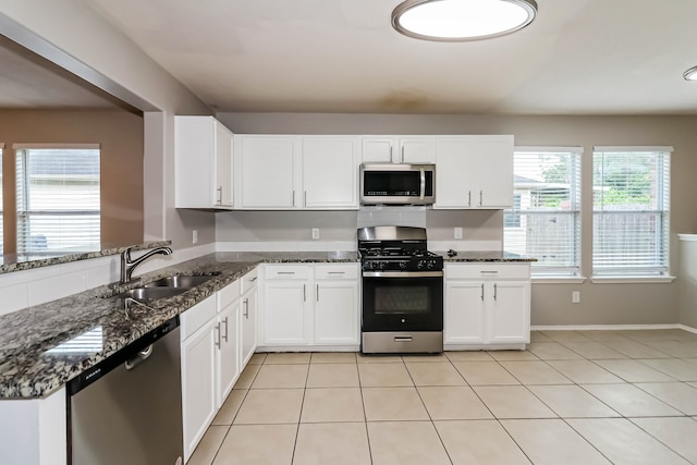 kitchen featuring stainless steel appliances, sink, dark stone countertops, white cabinets, and light tile patterned flooring