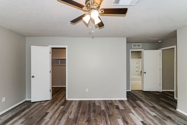 unfurnished bedroom featuring connected bathroom, ceiling fan, a closet, dark wood-type flooring, and a walk in closet