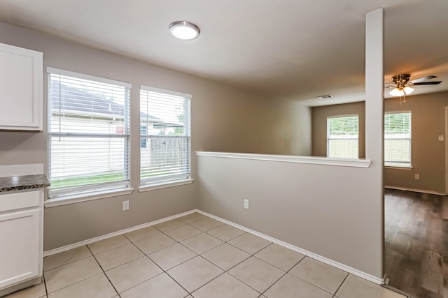 empty room with ceiling fan, light tile patterned floors, and plenty of natural light