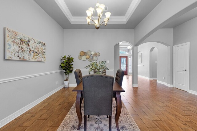 dining space featuring ornamental molding, an inviting chandelier, a raised ceiling, and hardwood / wood-style floors