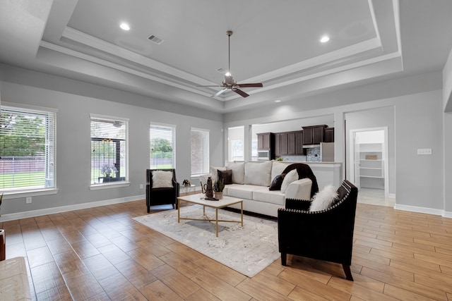 living room featuring a wealth of natural light, a tray ceiling, ceiling fan, and light hardwood / wood-style floors