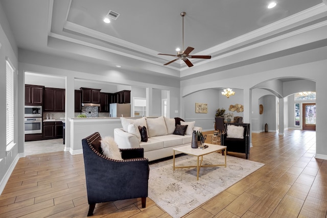 living room with ornamental molding, ceiling fan with notable chandelier, a tray ceiling, and light hardwood / wood-style flooring