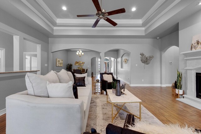 living room featuring light hardwood / wood-style flooring, a tiled fireplace, a raised ceiling, and ornamental molding