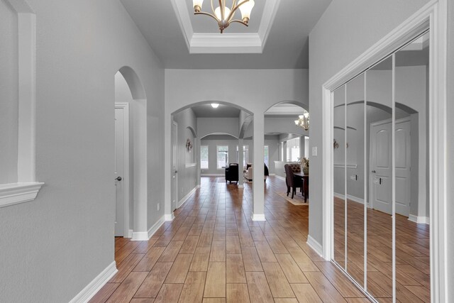 corridor with a notable chandelier, a raised ceiling, crown molding, and light hardwood / wood-style floors