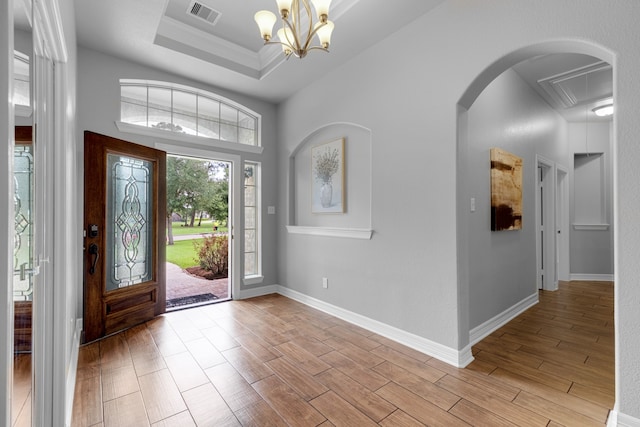 entrance foyer featuring an inviting chandelier, light wood-type flooring, crown molding, and a raised ceiling