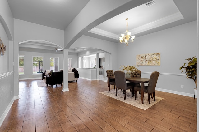 dining space featuring wood-type flooring, ceiling fan with notable chandelier, and a raised ceiling