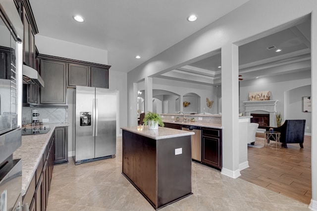 kitchen featuring appliances with stainless steel finishes, light hardwood / wood-style floors, light stone counters, a kitchen island, and dark brown cabinetry