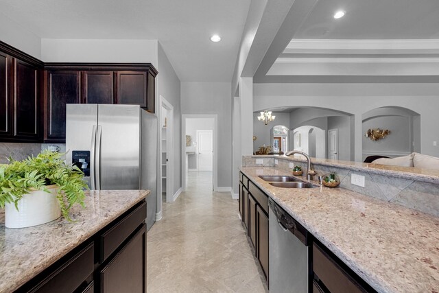 kitchen featuring sink, dark brown cabinets, stainless steel appliances, light stone countertops, and decorative backsplash