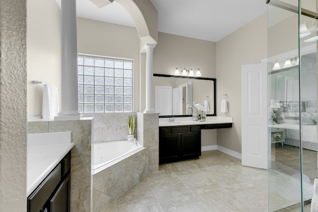 bathroom with decorative columns, tiled tub, and vanity