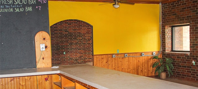 interior space featuring ceiling fan, wooden walls, and brick wall