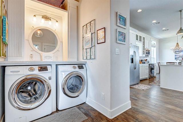 laundry area with dark wood-style floors, independent washer and dryer, visible vents, and an inviting chandelier