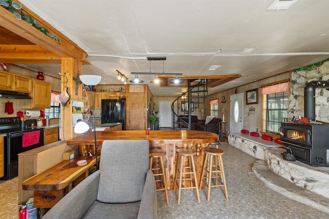 kitchen with a wood stove, black appliances, carpet, and wooden walls