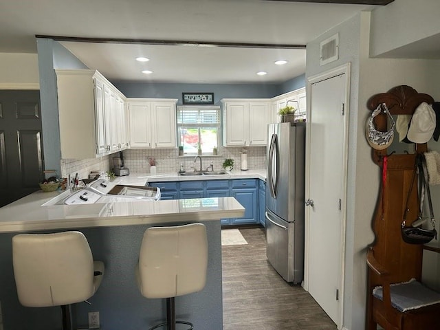 kitchen featuring a kitchen bar, kitchen peninsula, blue cabinets, white cabinetry, and stainless steel refrigerator