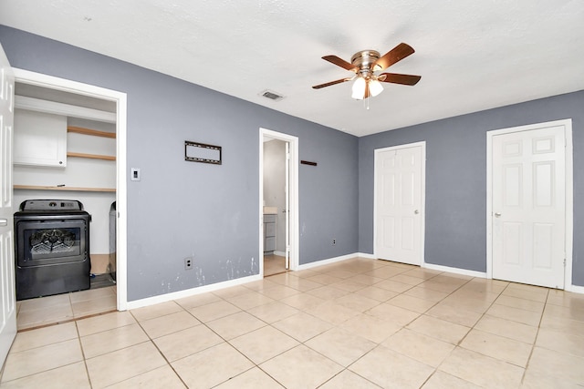 unfurnished bedroom with washer / dryer, ensuite bathroom, ceiling fan, and light tile patterned flooring