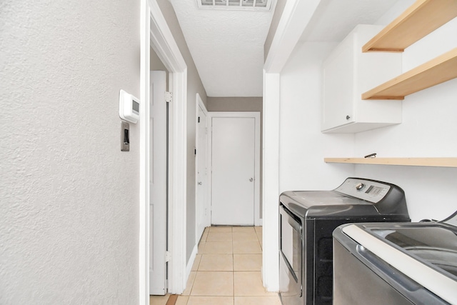 laundry area with a textured ceiling, cabinets, washing machine and dryer, and light tile patterned floors