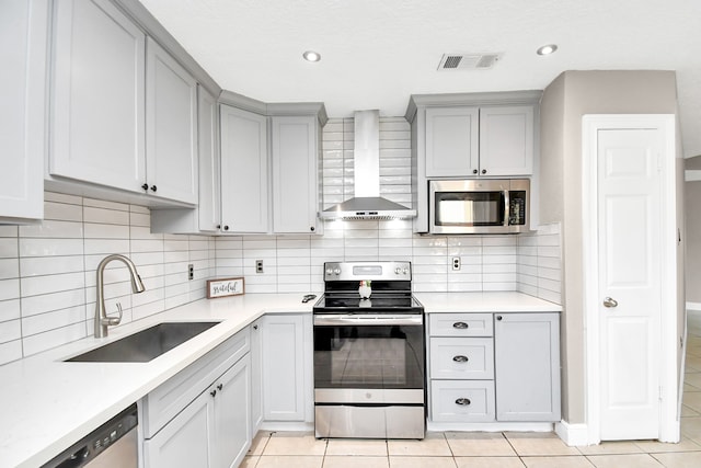 kitchen with wall chimney exhaust hood, light tile patterned floors, backsplash, appliances with stainless steel finishes, and sink